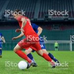 Football player challenging for ball on field during match.