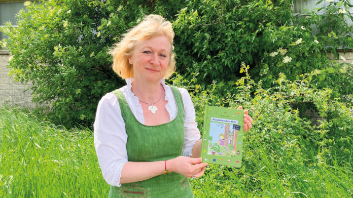 (C) Berger: Barbara Našel und ihr Kinderbuch. Im Hintergrund: eine Wildrose.