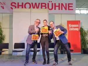 (C) zVg: Chefredakteur Hans Steiner (r.) und Sportjournalist Bobby Sommer (l.) suchen den nächsten Bezirkskaiser. Schiedsrichterin Sandra (m.) überwacht das Bezirkskaiser-Quiz.