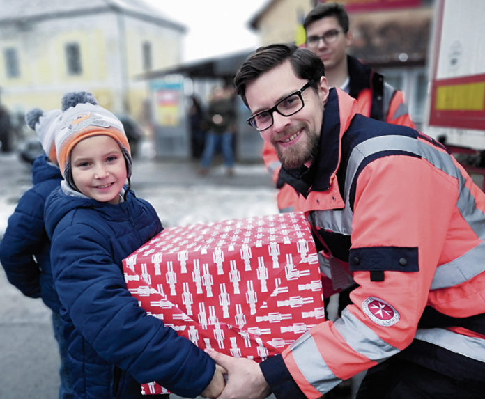 (C) Johanniter: Ein Johanniter-Helfer übergibt einem rumänischen Kind ein Packerl voll Lebensmittel.