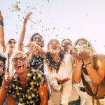 People having fun in party celebration friends concept – group of young and adult women all together laughing blowing coloured confetti – friendship and love for lifestyle with mixed active generations