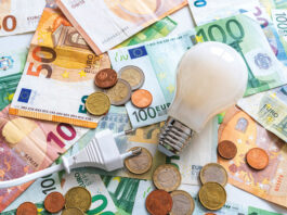 Glühbirne Stromkabel vor Euro-Scheinen und Euro-Münzen