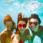Cheerful friends making selfie underwater in pool