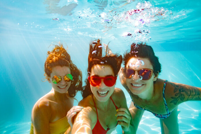 Cheerful friends making selfie underwater in pool