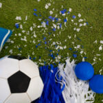 Overhead view of a blue and white soccer ball, vuvuzela and party favors on the playing field