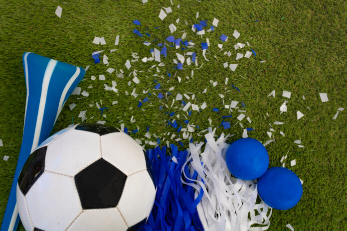Overhead view of a blue and white soccer ball, vuvuzela and party favors on the playing field