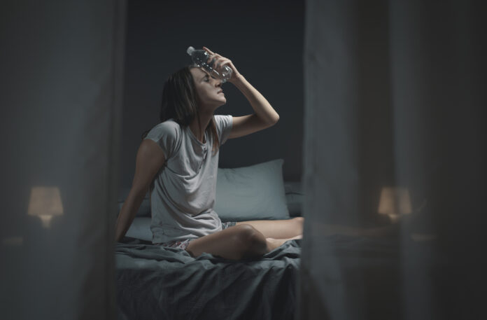 Frau sitzt im Bett weil heiß