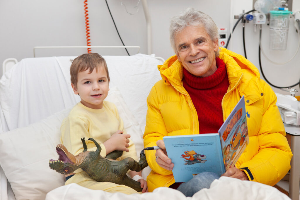 Thomas Brezina übergibt einem Kind das Weihnachtsbuch (Bild: Philipp Tomsich/Kinderfreunde).