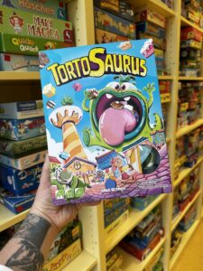 Tortosaurus (ab 6, Blue Orange): Ein taktisches Geschicklichkeitsspiel mit Humor: In einer Bäckerei sollen Torten ausgeliefert werden, während der gefräßige Tortosaurus Runde für Runde zuschlägt. Frisst er zu viel, kippt er um – und das Spiel endet für alle. © Peter Wieser